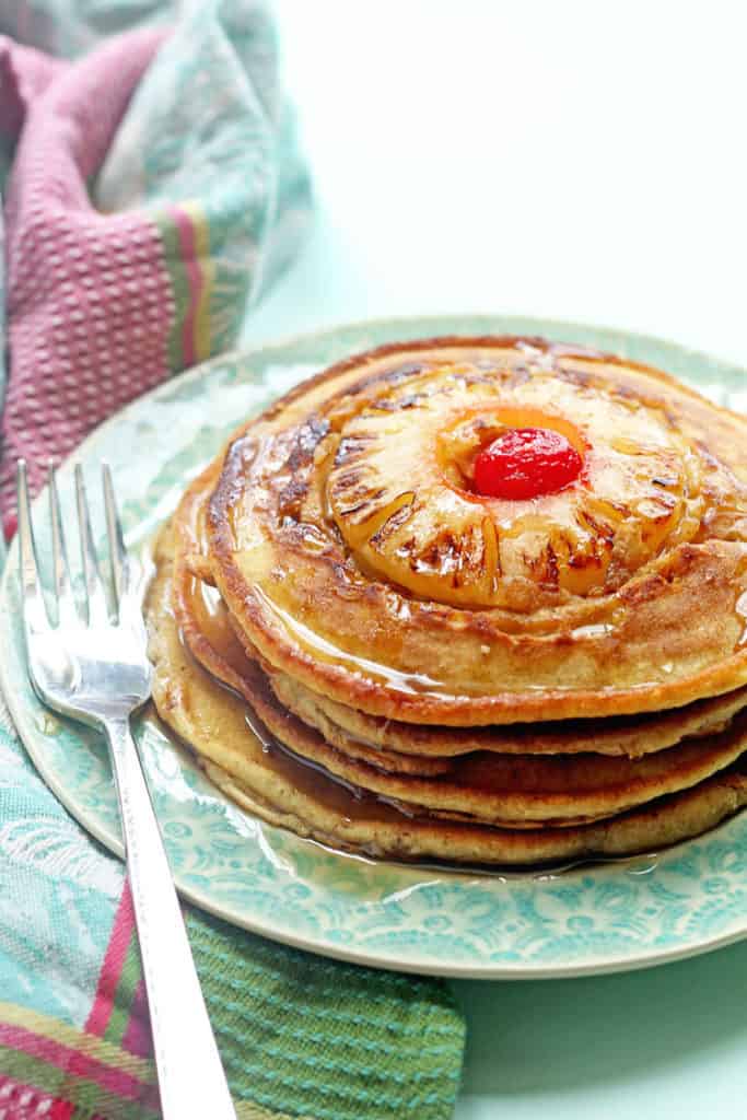 A stack of pineapple upside down pancakes topped with baked pineapple and cherry in the center