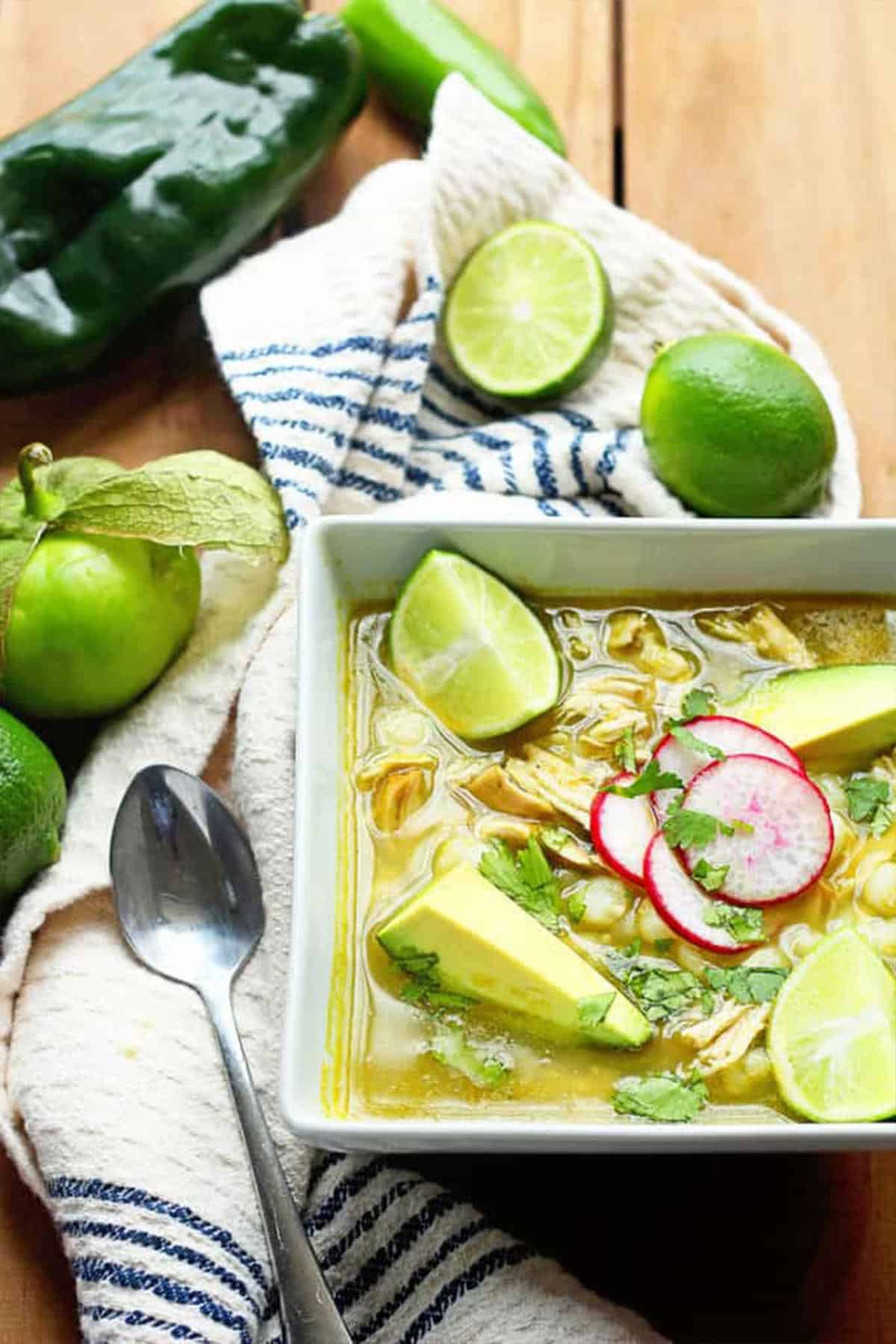 Green pozole chicken in a bowl with garnishes on top and a spoon to the side.