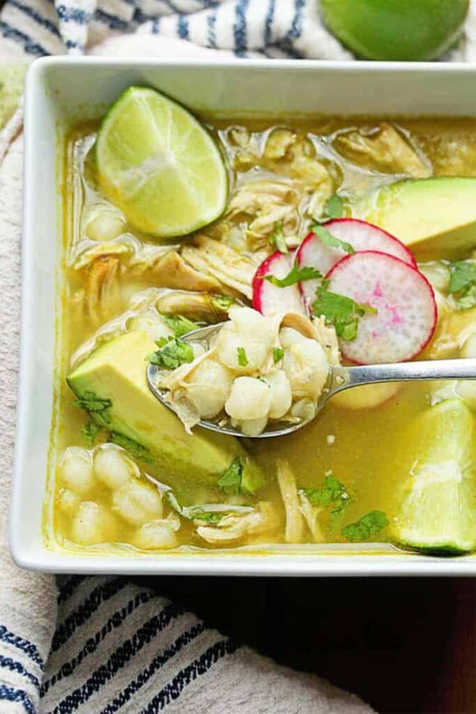 Close up of Chicken Pozole Verde Recipe in large white bowl with spoon digging in