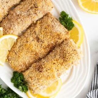 Overhead shot of several lemon panko crusted fish fillets on a white serving platter, garnished with parsley and lemon slices