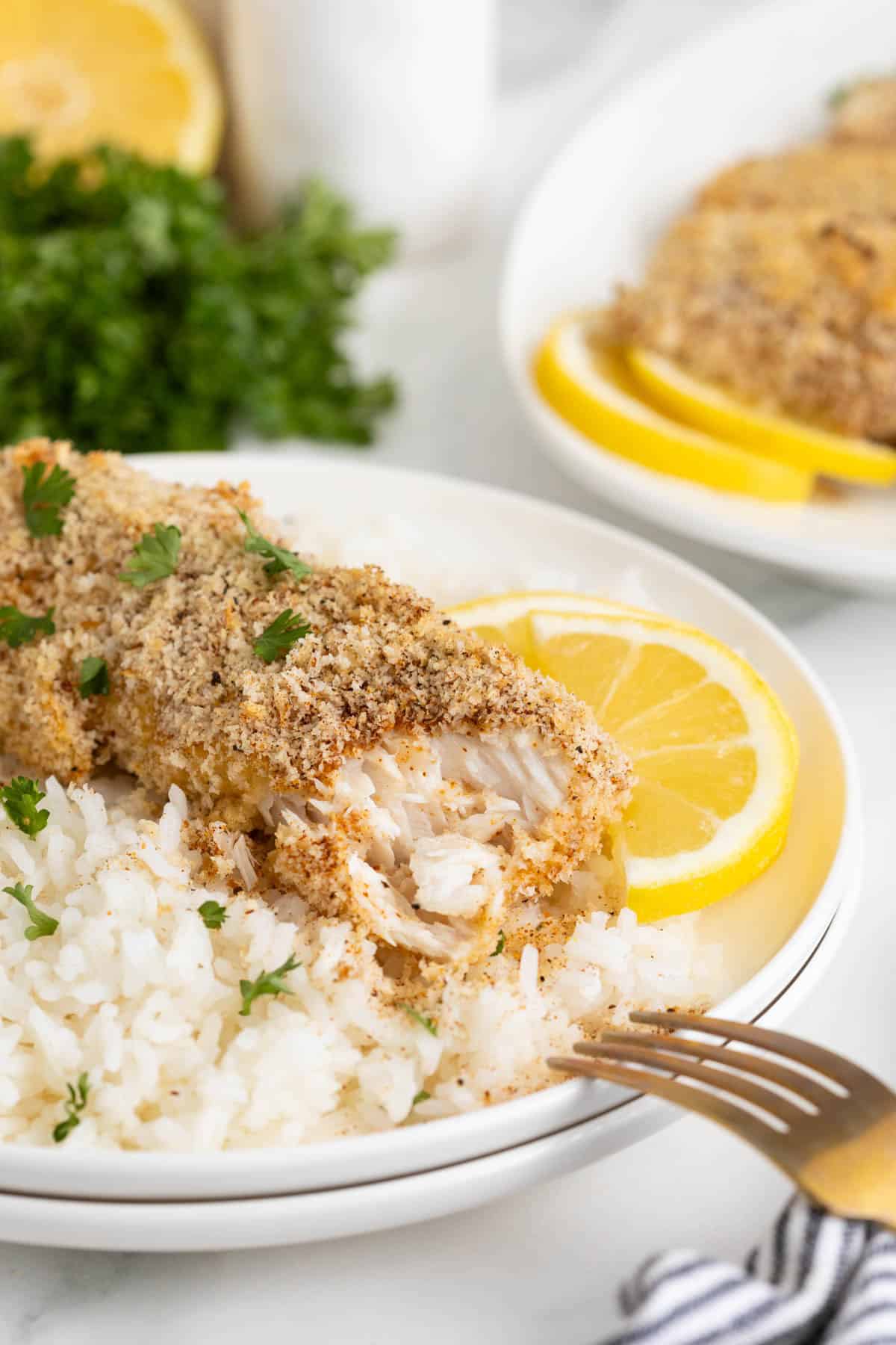 Bite taken out of a crispy lemon panko crusted fish fillet served over white rice with lemon slices, showing the flaky interior
