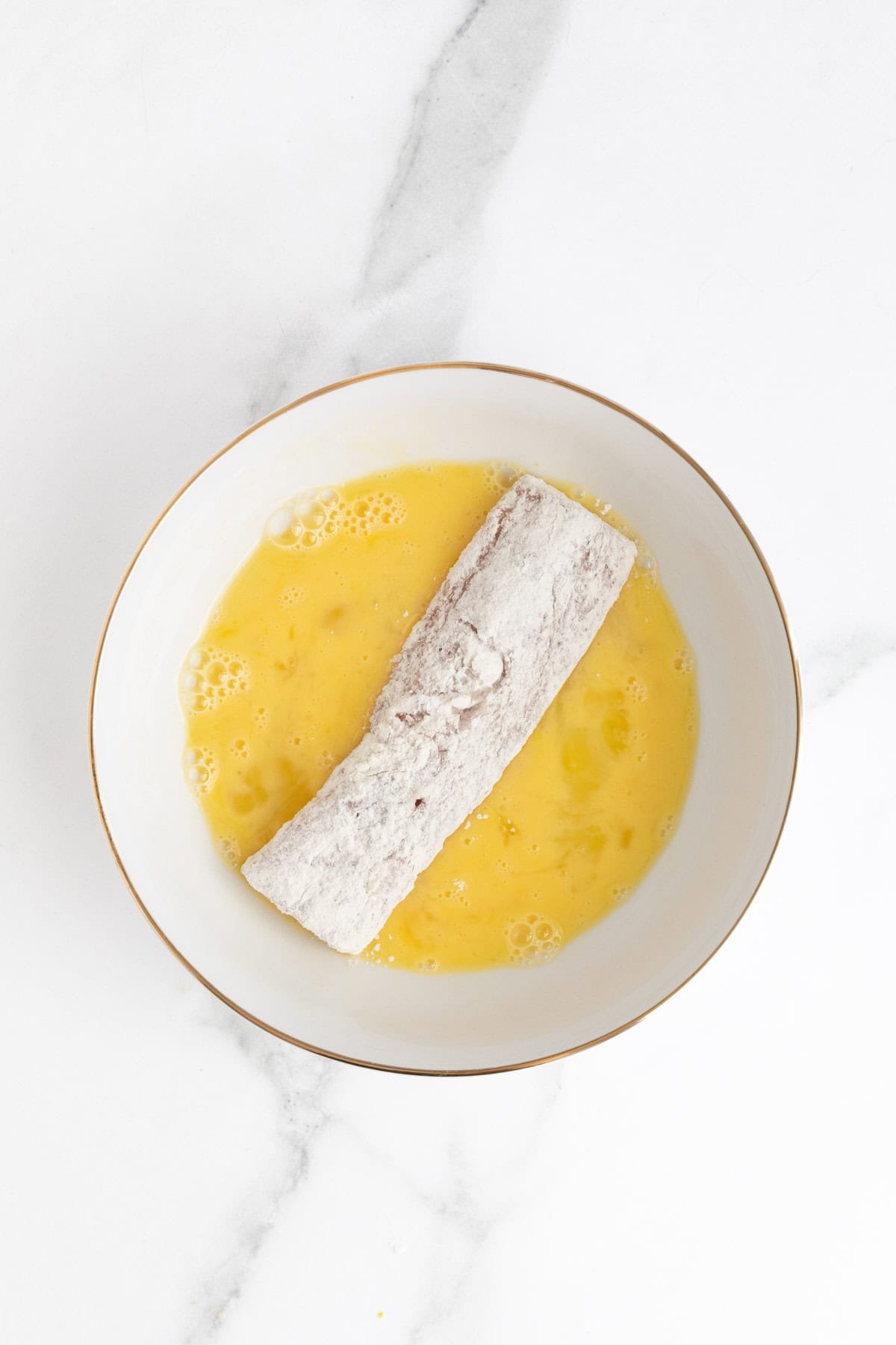 Floured fish fillet being dipped into the bowl of beaten eggs