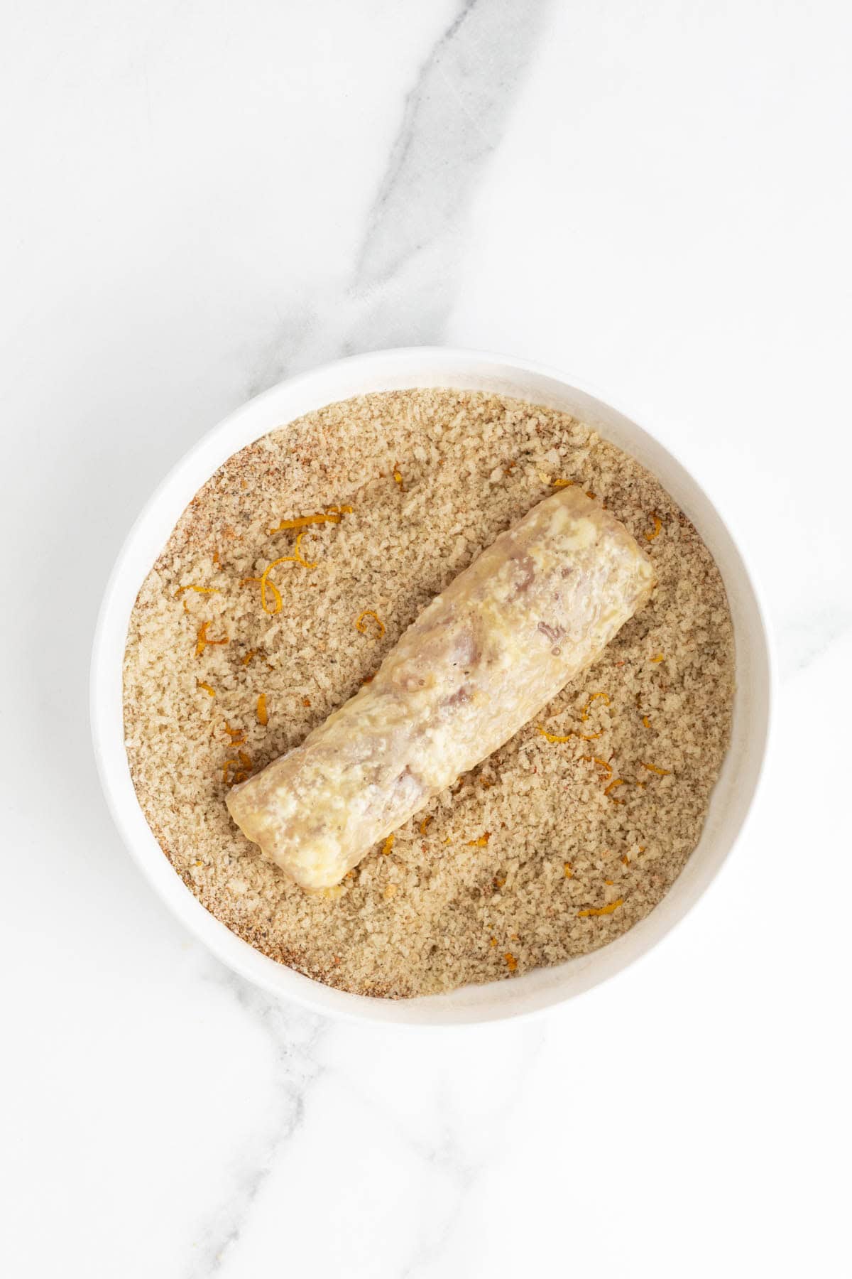 Raw fish fillet coated in egg, resting in a bowl of seasoned panko crumbs