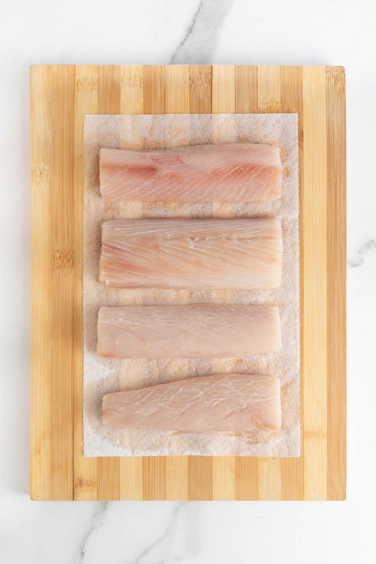 Four raw fish fillets laid out on a wooden cutting board with paper towels