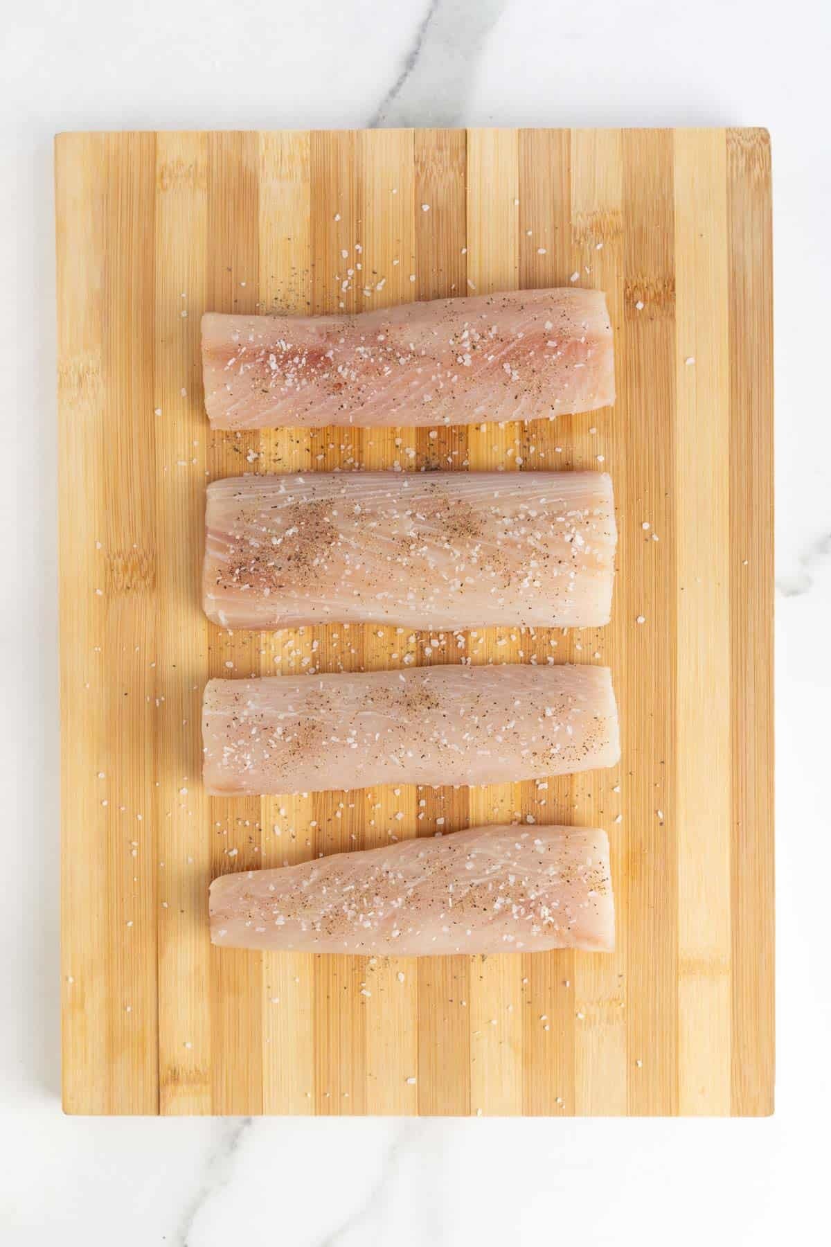 Fish fillets on a cutting board, seasoned with salt and pepper