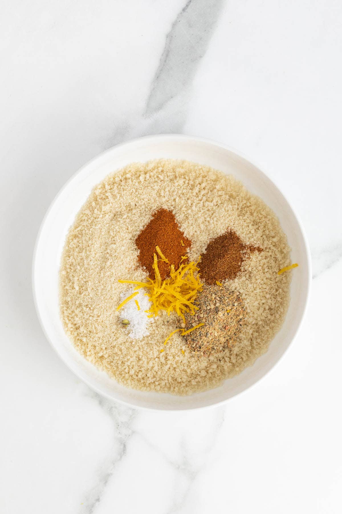 White bowl filled with panko breadcrumbs, spices, and lemon zest before mixing