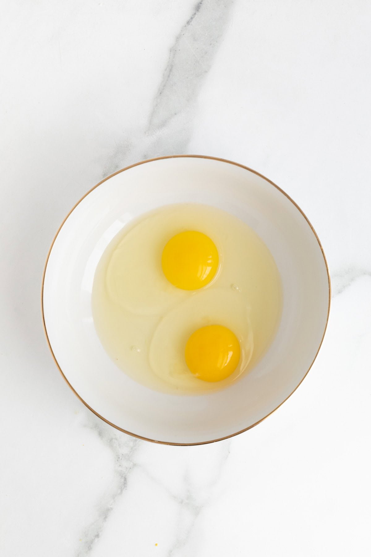 Two raw eggs cracked into a white bowl, ready for whisking