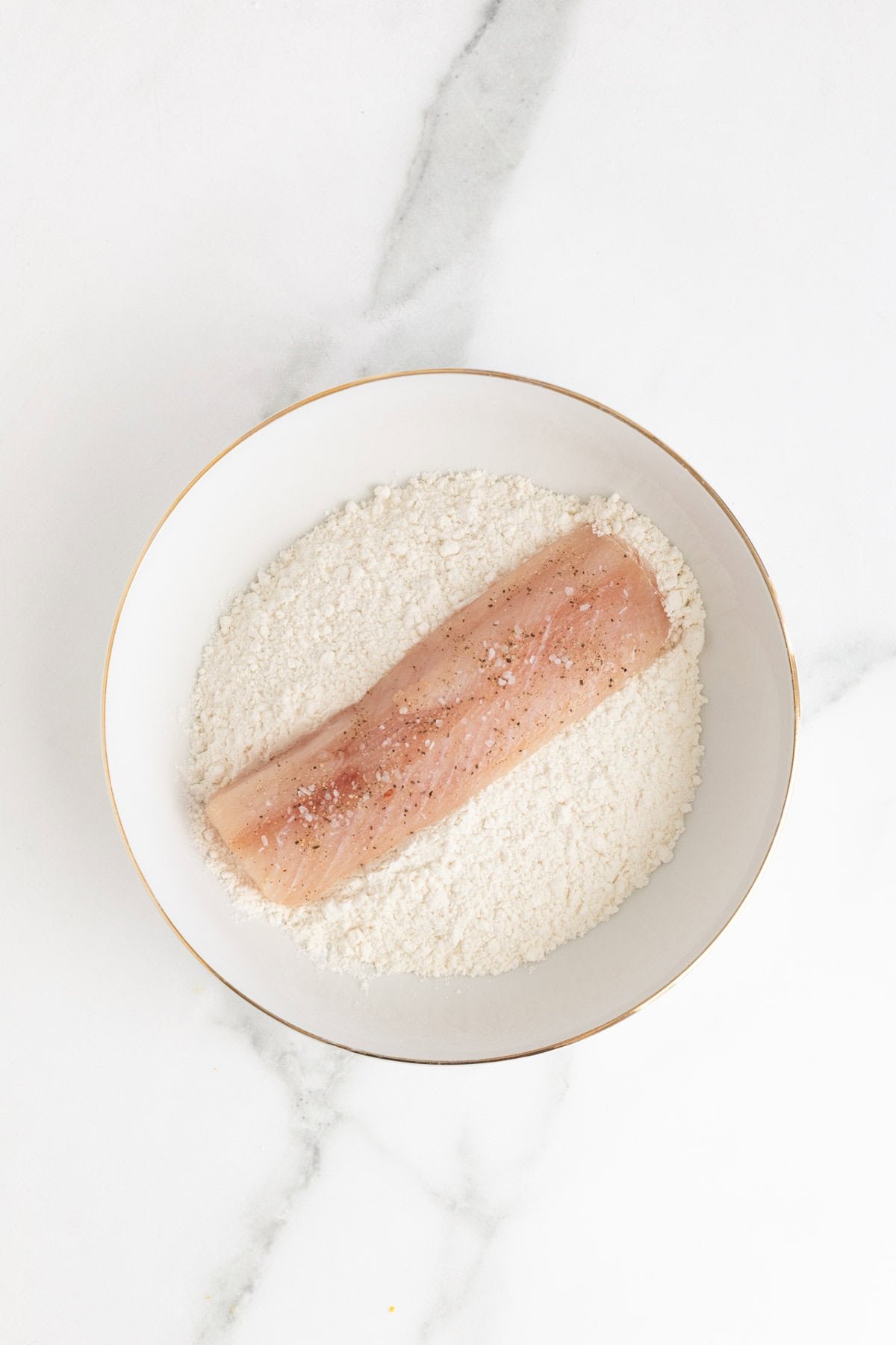 Seasoned fish fillet placed into the bowl of flour