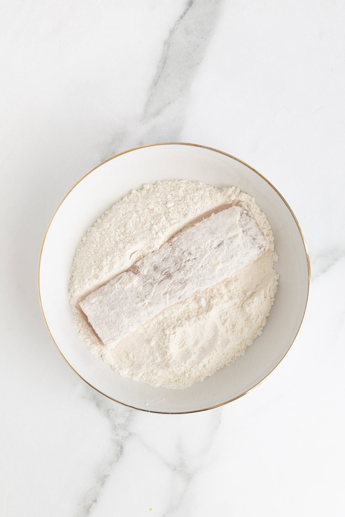 Fish fillet fully coated in flour inside the bowl