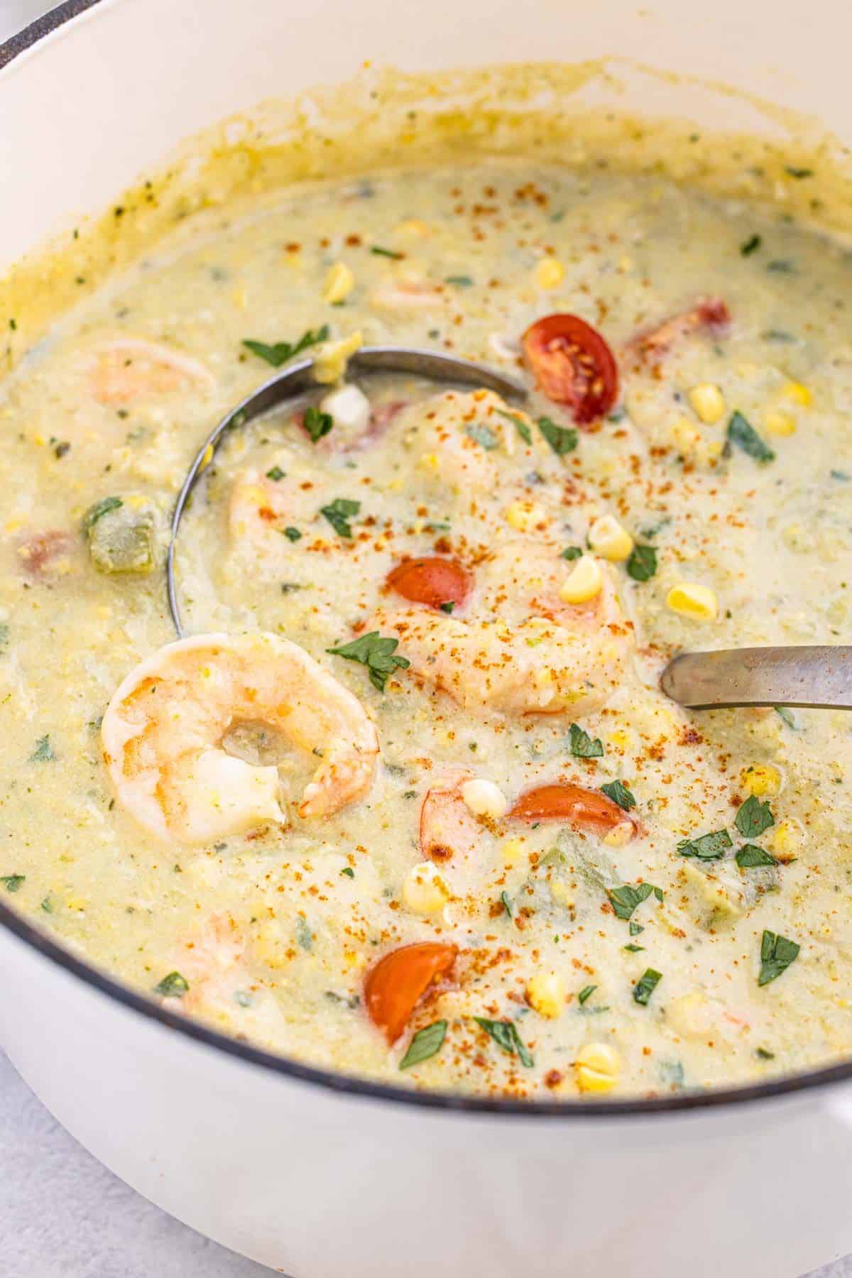 A ladle scooping up a serving of shrimp and corn chowder.