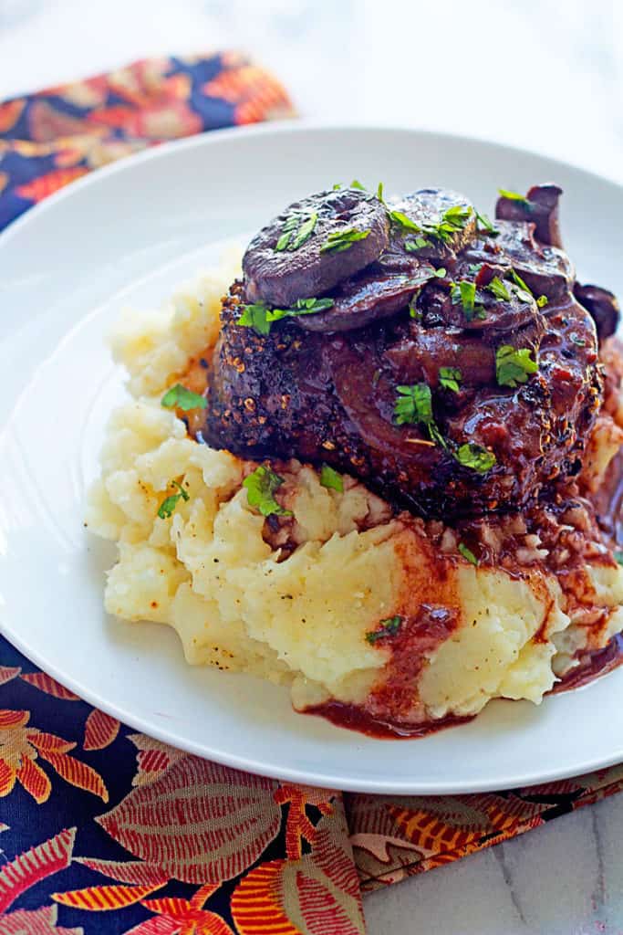 Peppercorn Crusted Filet Mignons served with creamy mashed potatoes beneath and topped with gravy on a round, white plate