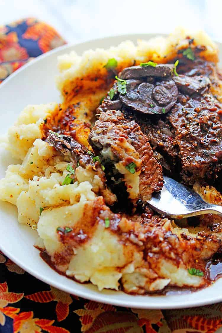 Peppercorn Steaks being cut into with a fork with a red wine sauce served on top of mashed potatoes. 