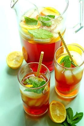 Overhead shot of sweet tea contained in a pitcher and two glasses with straws all garnished with lemon wedges and mint