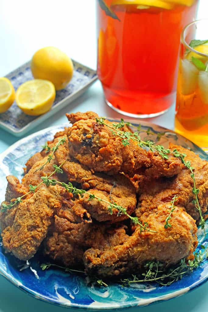 A pile of sweet tea fried chicken next to a pitcher and glass full of sweet tea and lemons