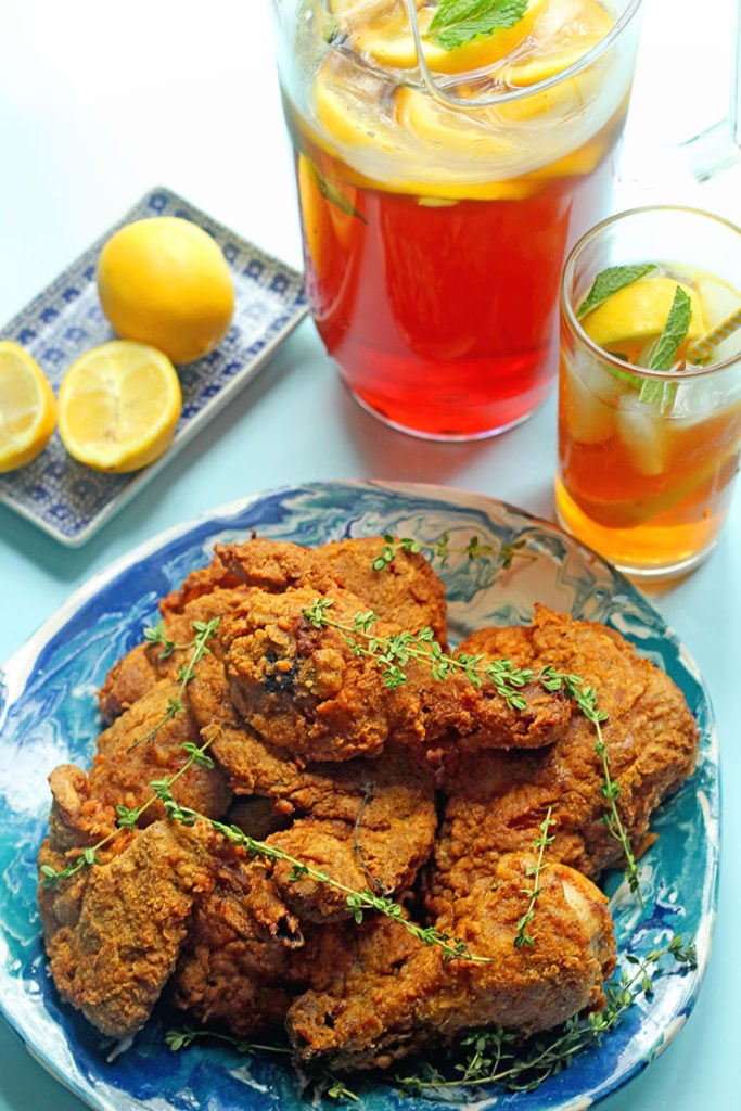 Overhead shot of a pile of sweet tea fried chicken next to a pitcher and glass full of sweet tea and lemons