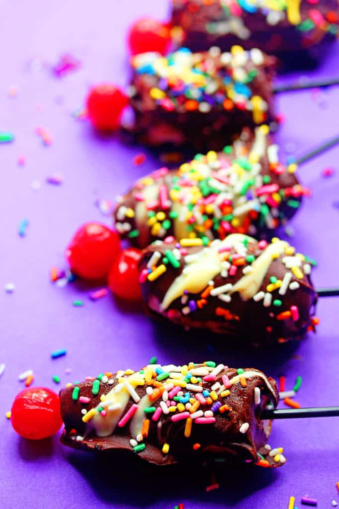 Close up of a row of banana split pops dipped in chocolate and topped with sprinkles and a cherry