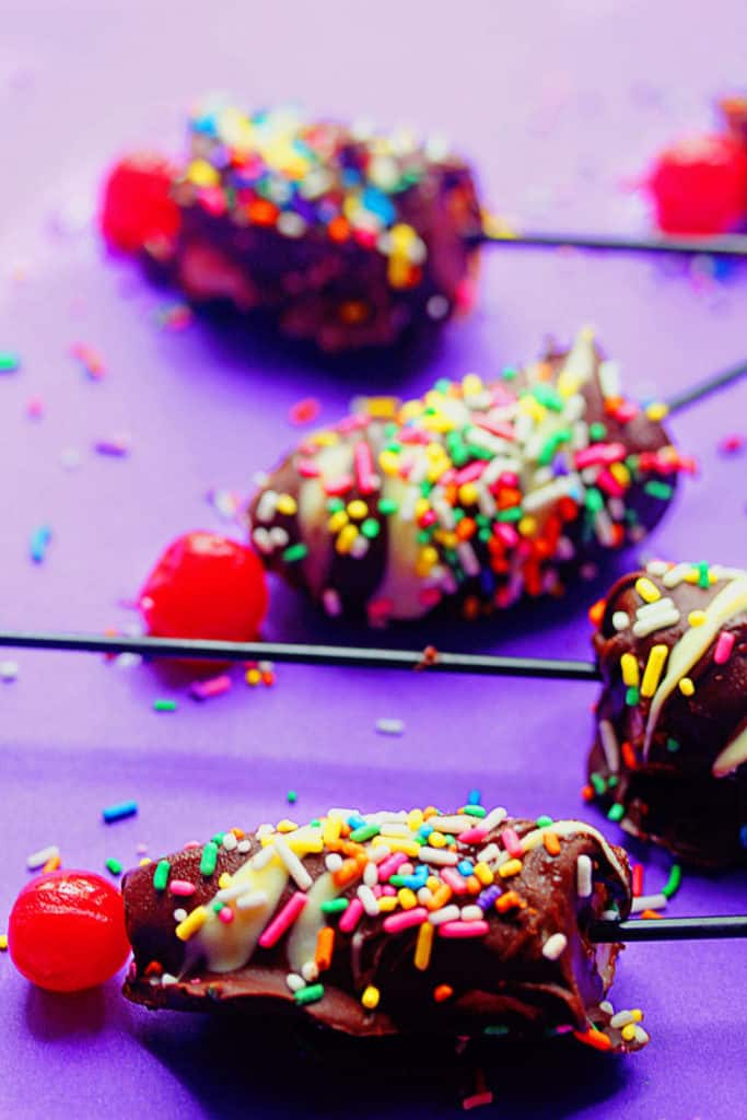 Banana split pops dipped in chocolate and topped with sprinkles and a cherry