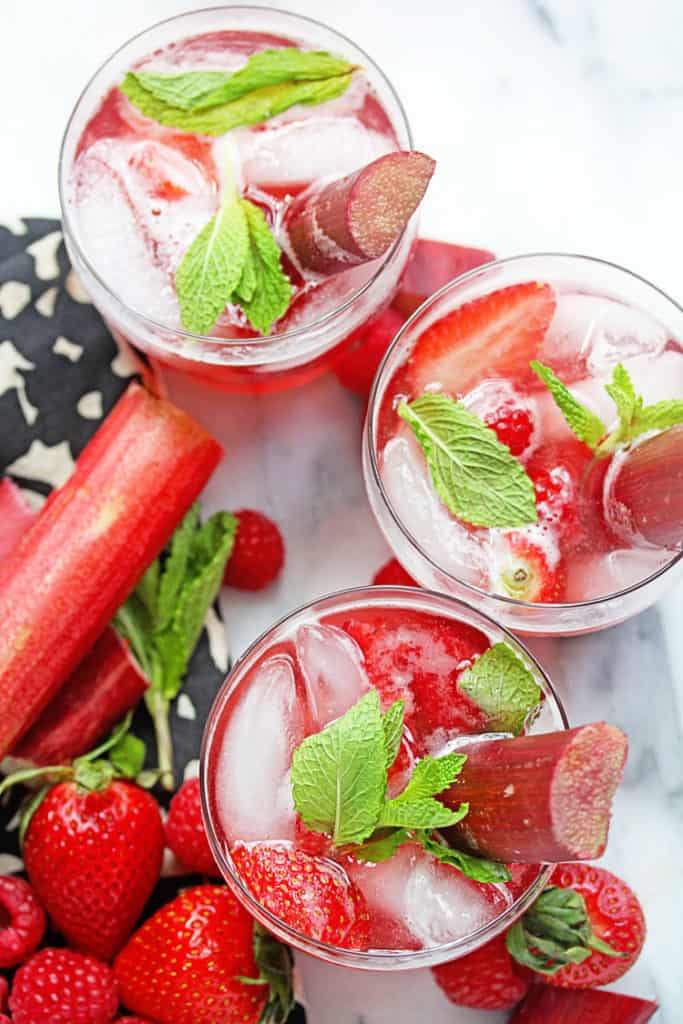 Overhead shot of three glasses of Berry Rhubarb Punch garnished with pieces of mint and rhubarb