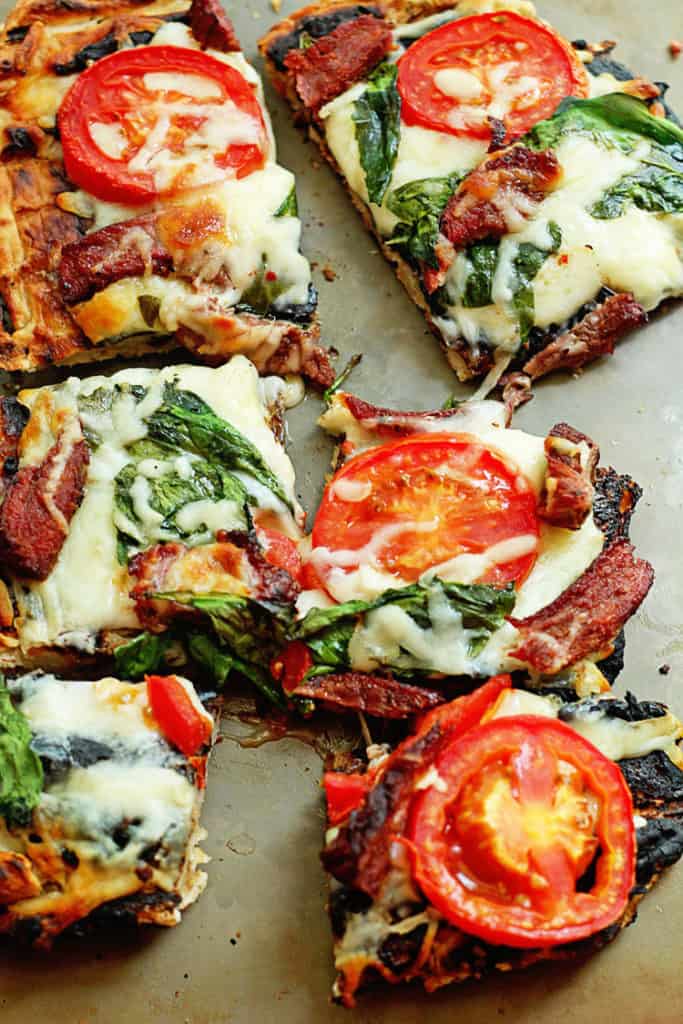Several pieces of Grilled Flank Steak Flatbread topped with cheese, spinach and tomatoes
