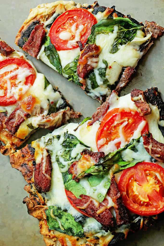 Close up of several pieces of Grilled Flank Steak Flatbread topped with cheese, spinach and tomatoes