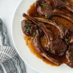 The best lamb chops in a glaze on a white round plate on white background with a napkin