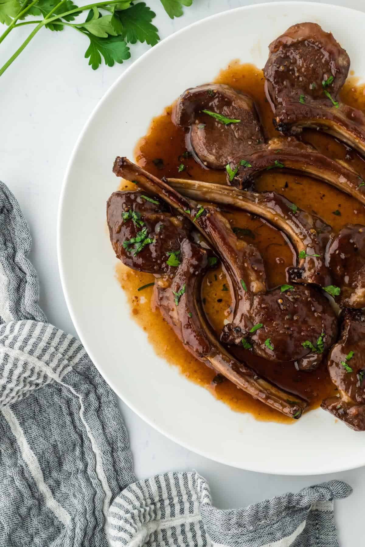 The best lamb chops in a glaze on a white round plate on white background with a napkin