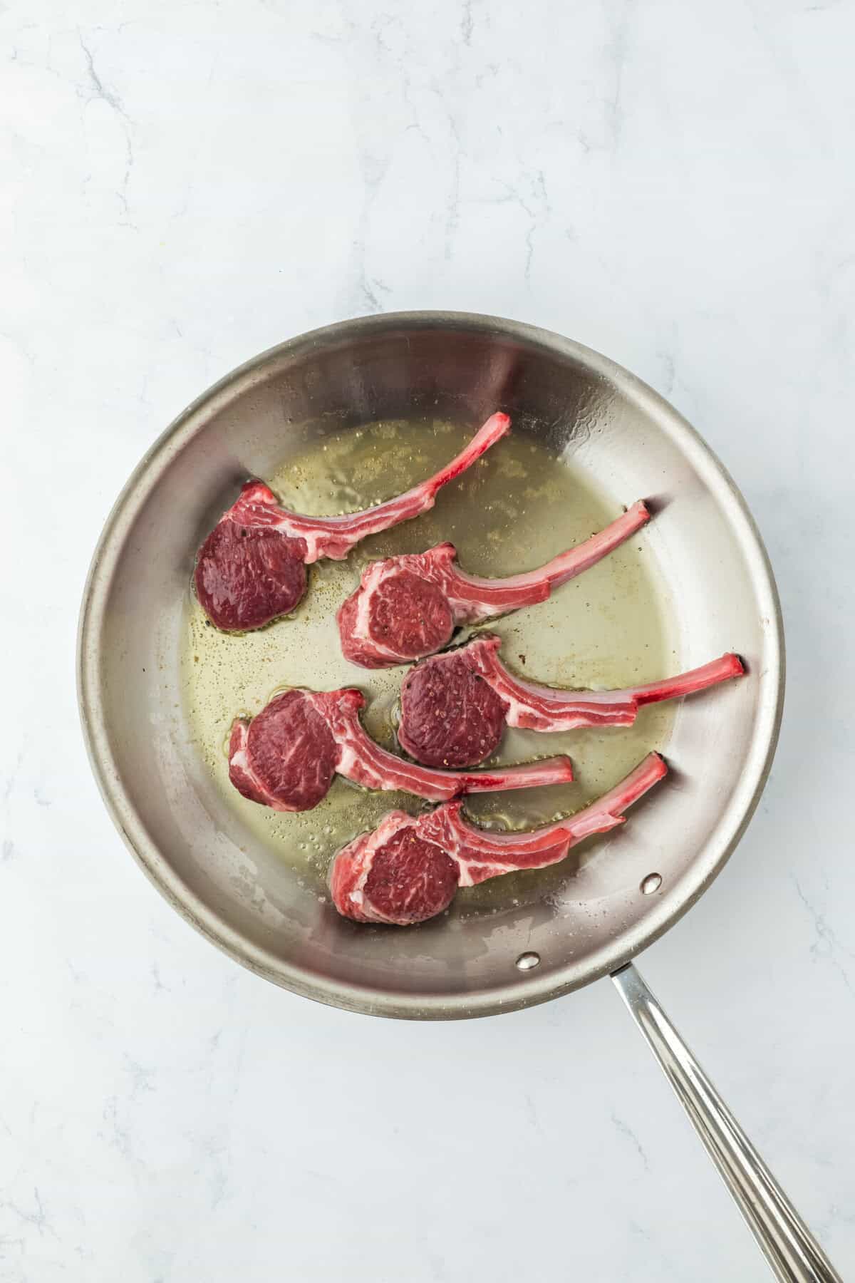 Lamb chops in a skillet with oil being seared