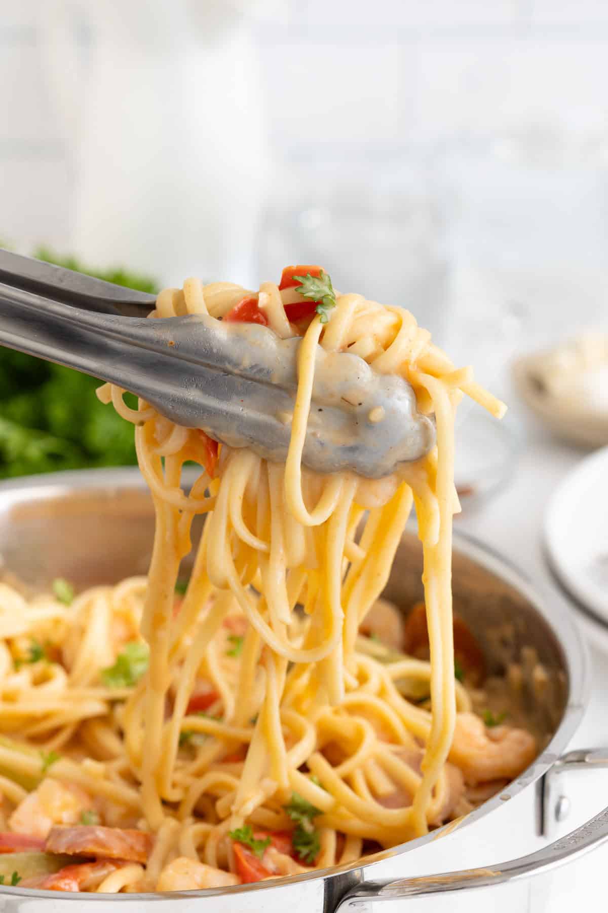 Tongs lifting a serving of Cajun shrimp pasta from the pot