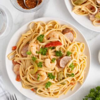 Overhead view of a plate of cajun shrimp pasta served with parsley garnish and surrounded by a bowl with cajun seasoning, more pasta, and silverware