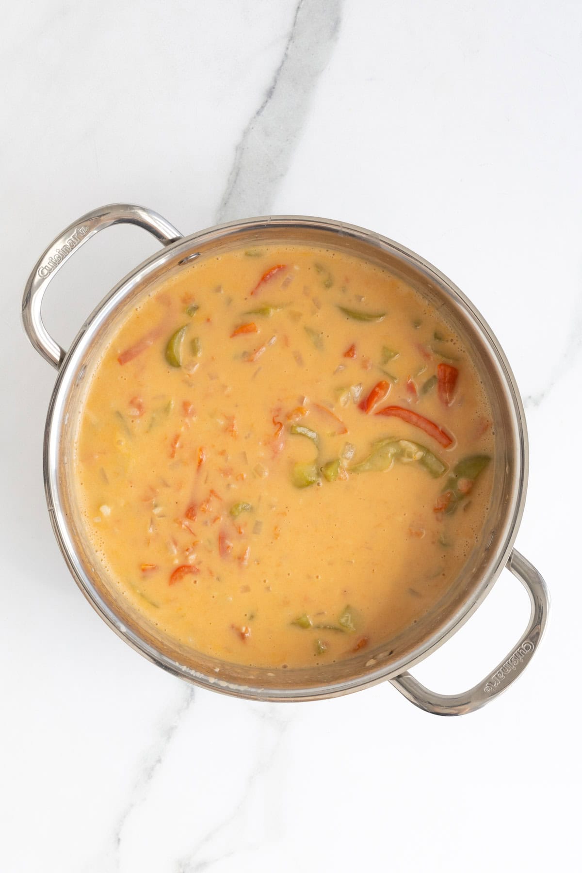 Creamy sauce with peppers simmering in a stainless steel pot