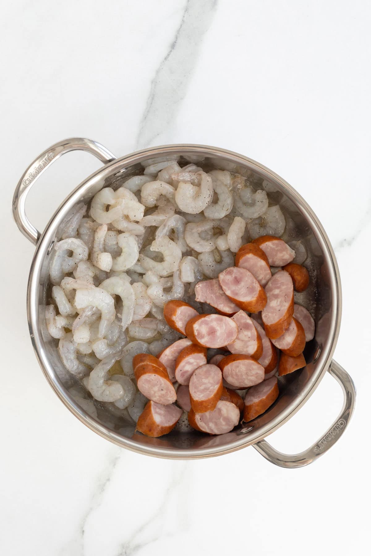 Raw shrimp and sliced sausage in a stainless steel pot before cooking