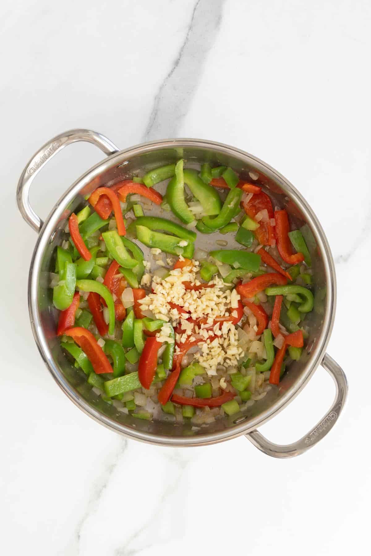 Chopped green and red bell peppers with garlic in a pot, ready to sauté