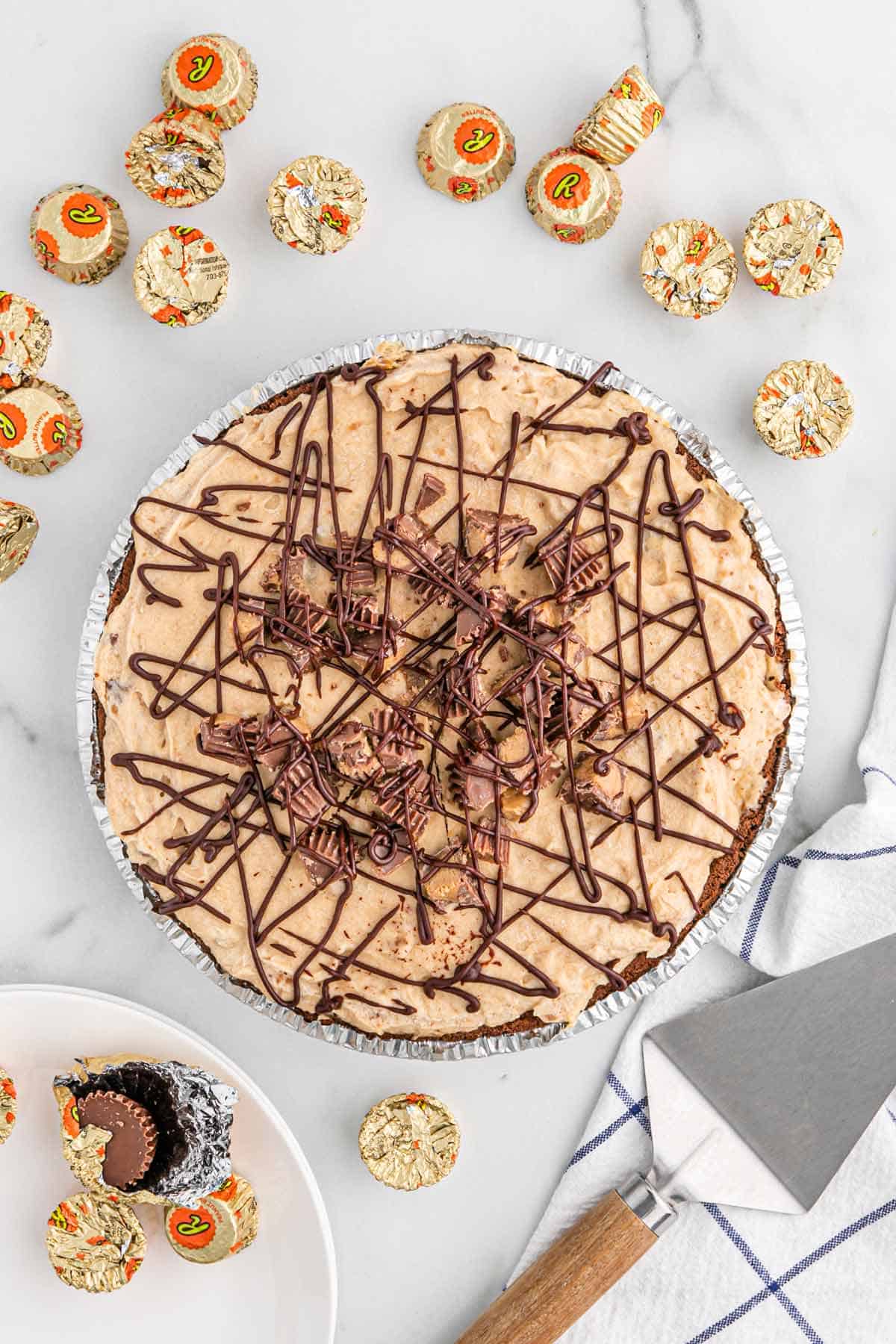 No bake peanut butter pie on the table with wrapped peanut butter cups around it.