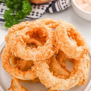 A plate of crispy fried onion rings on the table with sauce.