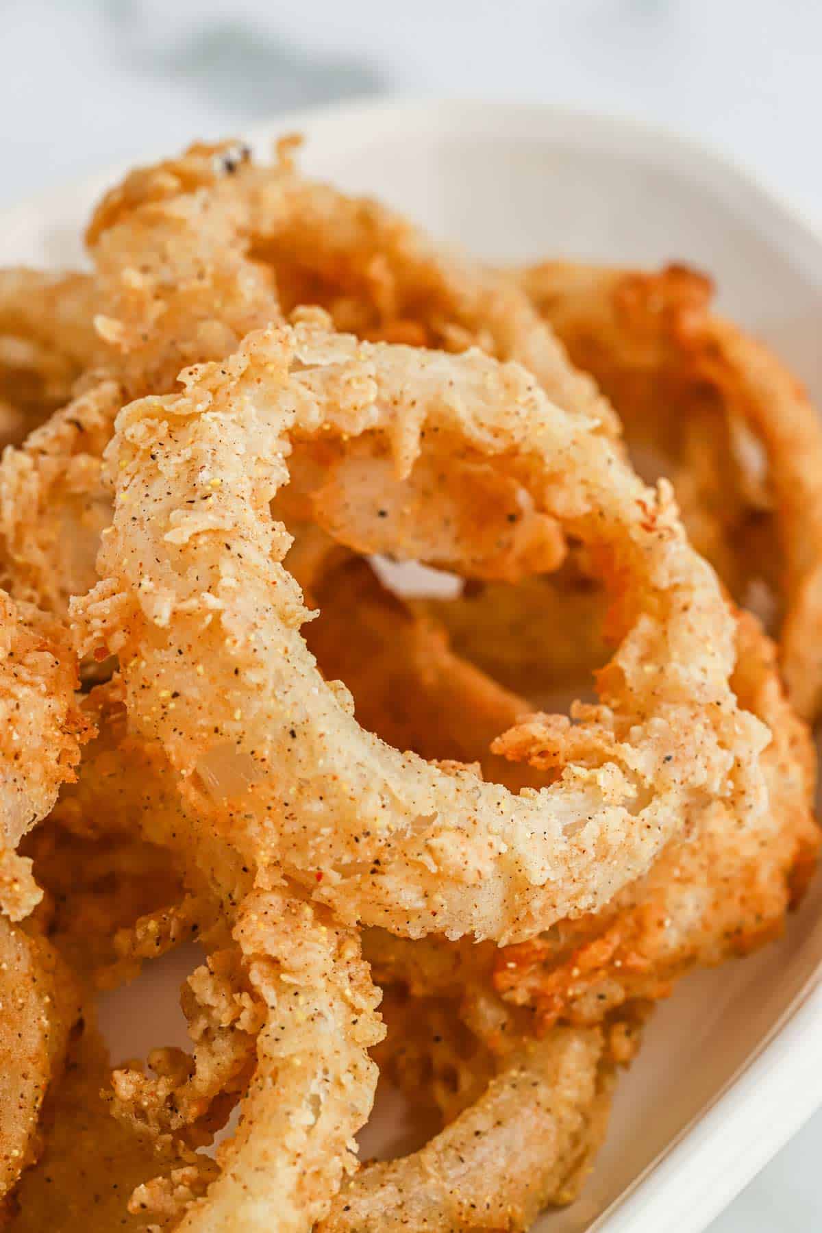 A closeup image of homemade fried onion rings piled on a plate.