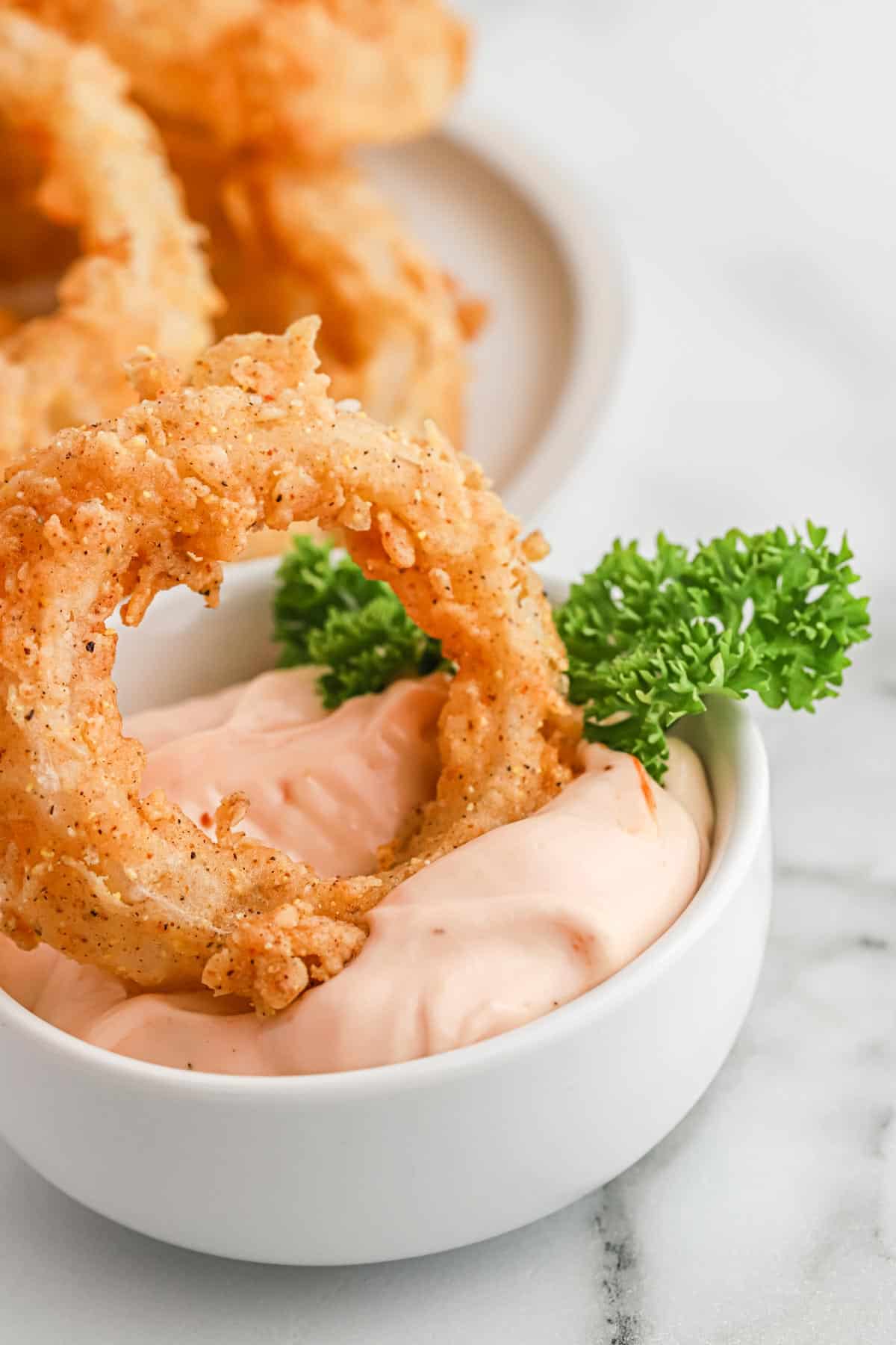 Dipping an onion ring into a pink sauce in a bowl.
