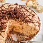 Peanut butter pie with oreo crust in a pie plate with pieces missing and peanut cups in the background.