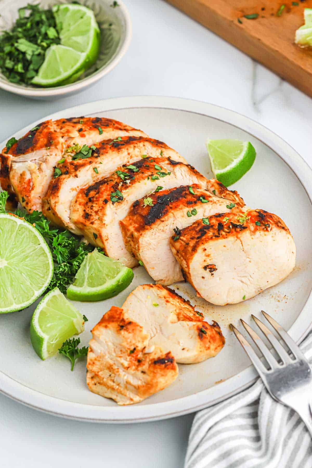 A plate of sliced grilled chicken garnished with cilantro and lime wedges.