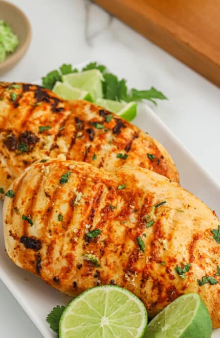Grilled tequila lime chicken on a plate with lime halves and cilantro.