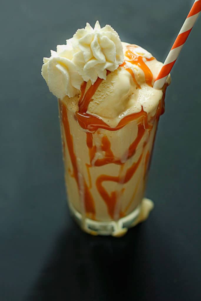 Caramel Bourbon Milkshake topped with whipped cream and served in a clear glass with an orange and white striped straw in it