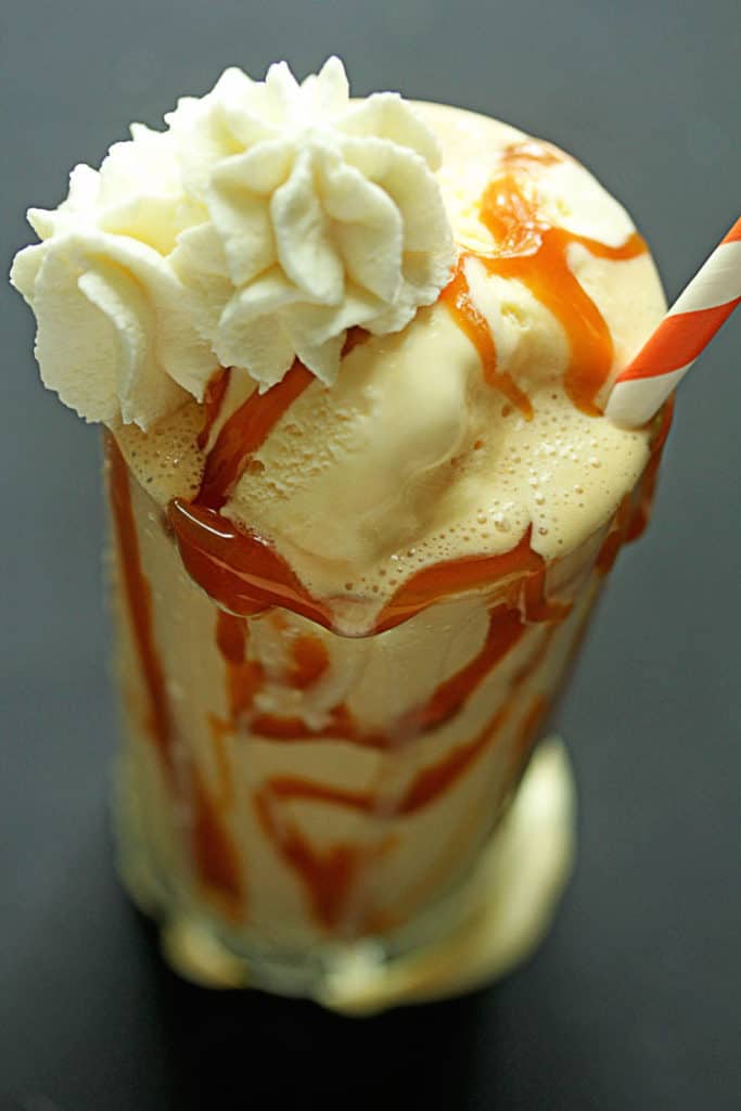 Overhead shot of a Caramel Bourbon Milkshake topped with whipped cream and served in a clear glass with an orange and white striped straw in it