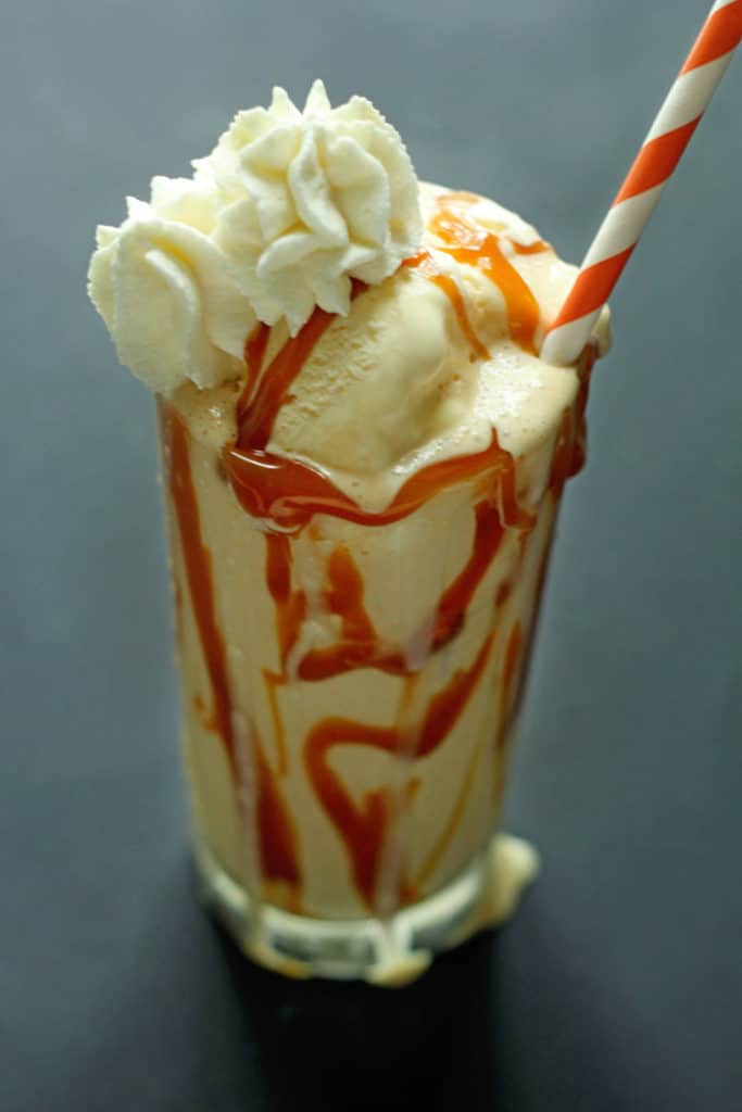 Caramel Bourbon Milkshake topped with whipped cream and served in a clear glass with an orange and white striped straw in it