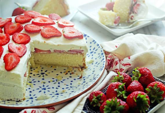A sliced strawberry yellow cake on a blue plate with strawberries on a server