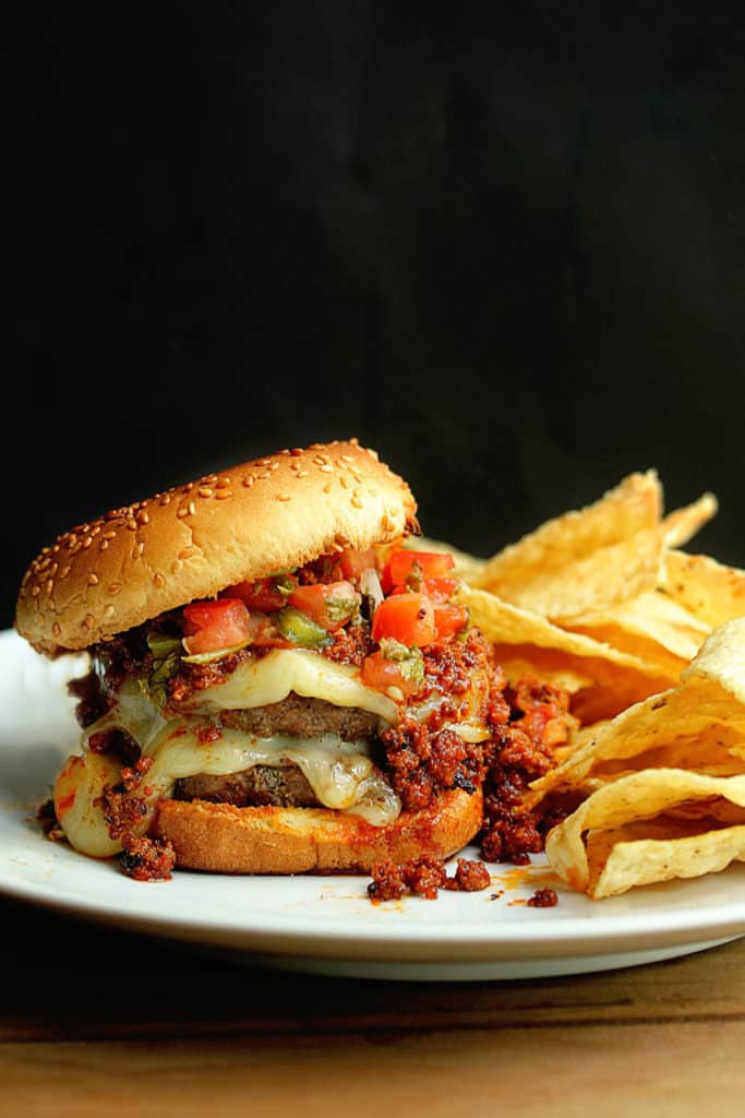 Piping hot latin burger served with tortilla chips on a white plate with a black background