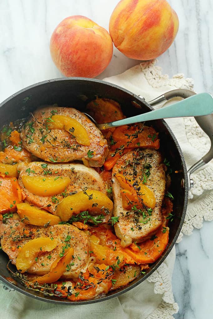 Pot full of Maple Peach Pork Chops topped with sliced peaches and fresh whole peaches next to it