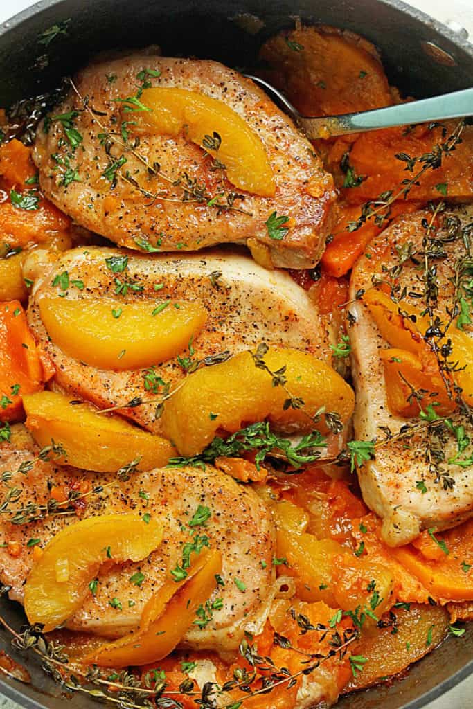 Close up of a pot full of Maple Peach Pork Chops topped with sliced peaches and a spoon in it