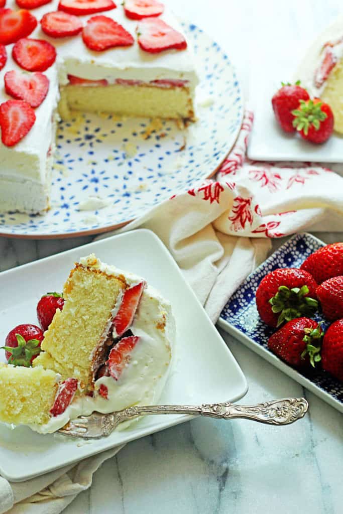 A strawberry yellow cake with a slice on a white plate with fork in the slice ready to serve