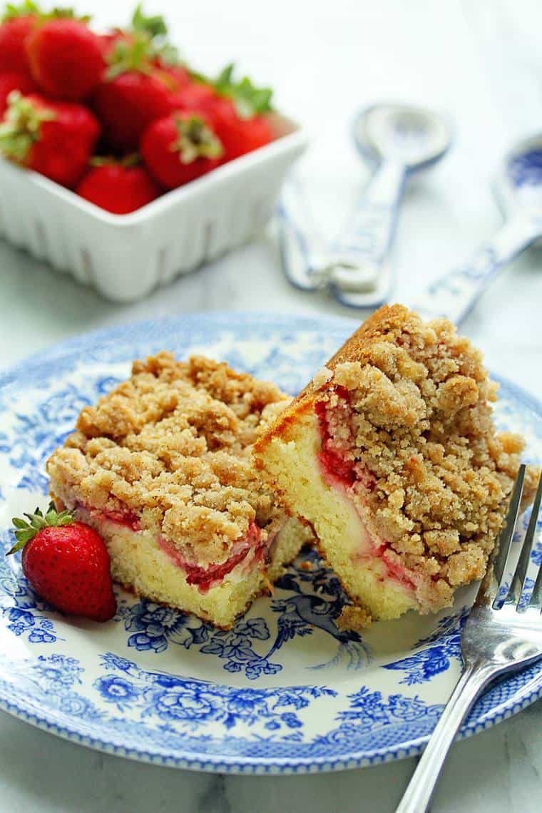 Strawberry Crumble Cake slices on a blue and white plate with fresh strawberries in background