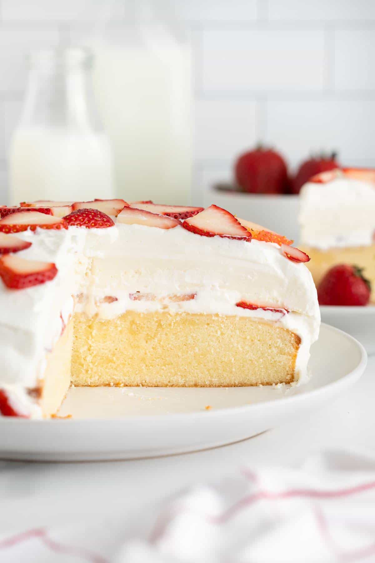 A side view of the strawberry shortcake cheesecake with a portion removed, revealing its moist interior layers and creamy whipped topping