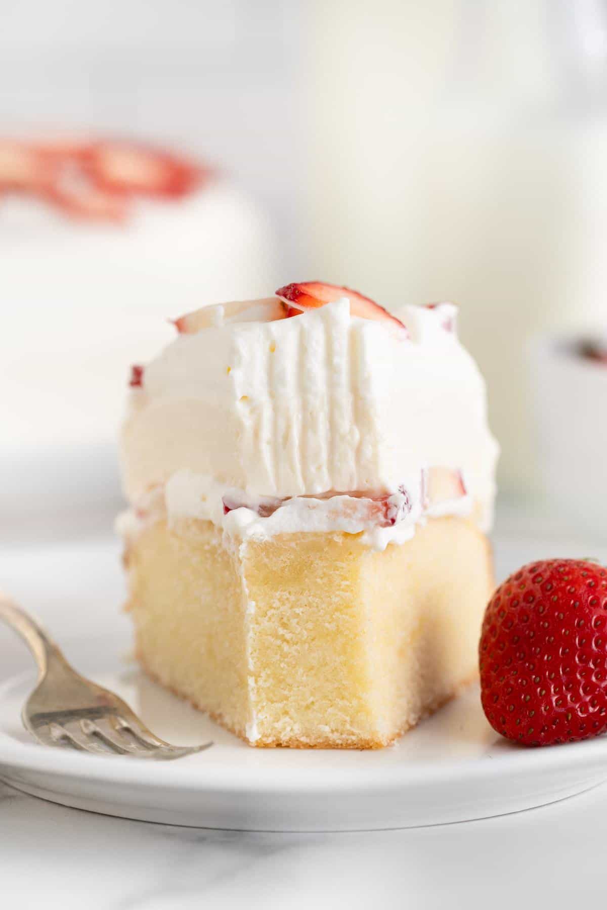 A close-up of a slice of strawberry shortcake cheesecake with a fork mark, with a strawberry and a fork next to it